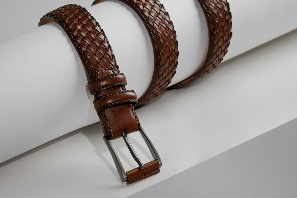 a pair of brown leather belts sitting on top of a white piece of paper; illustrative stock photograph
