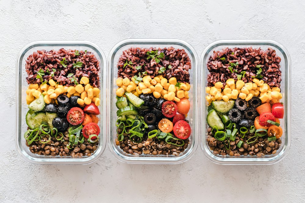 Three glass containers filled with rice, corn, olives, tomatoes, cucumbers, and lentils; illustrative stock photograph