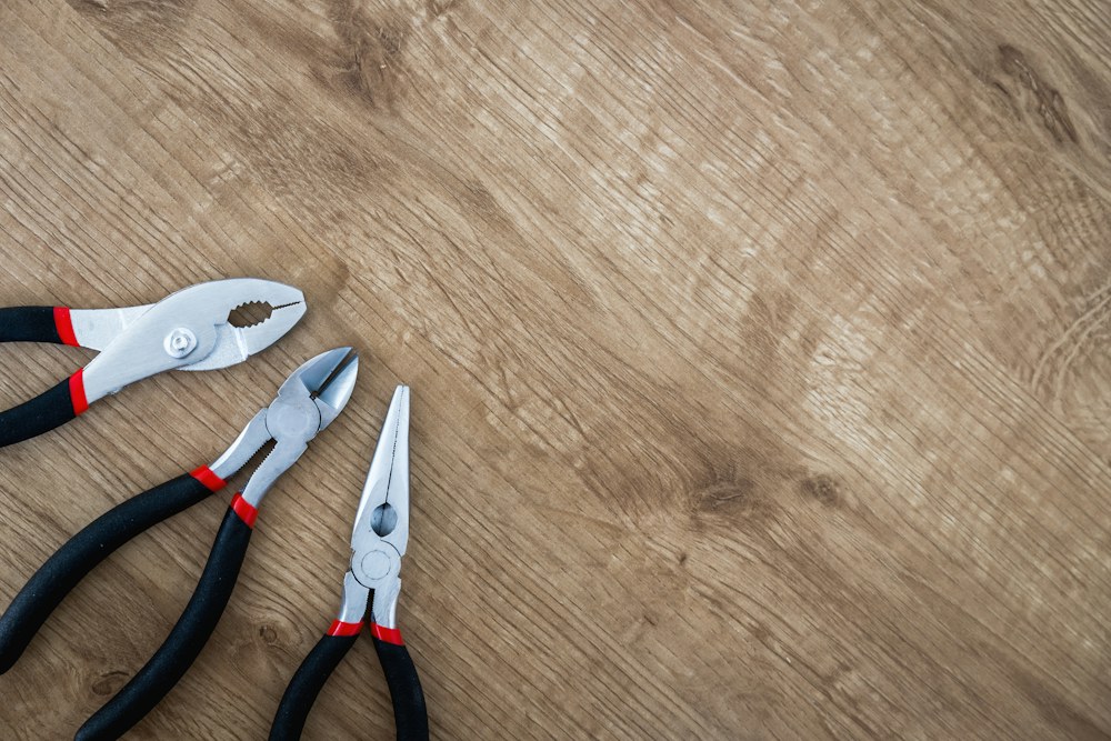 three black handled pliers on brown surface; illustrative stock photograph