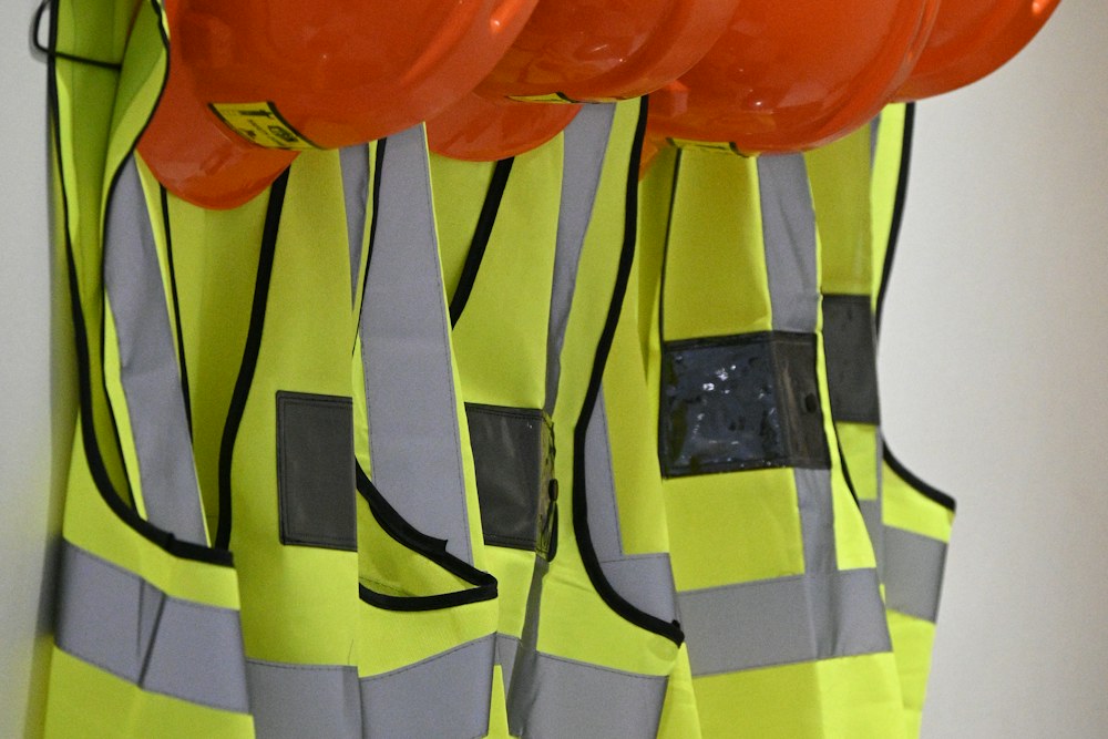 Four orange hard hats and neon yellow safety vests hanging on a wall; illustrative stock photograph